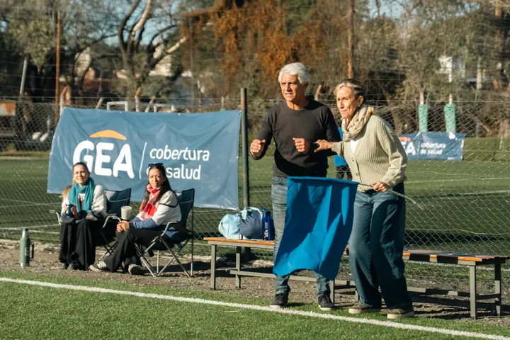 Abuelos alentando en la cancha de fútbol, junto a un cartel de GEA cobertura de salud